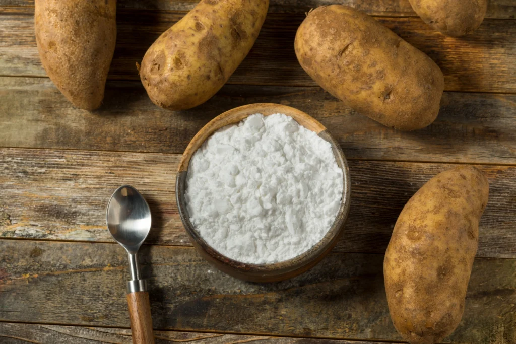 Raw potatoes next to a bowl of pure white potato starch representing resistant starch prebiotics for gut bacteria.
